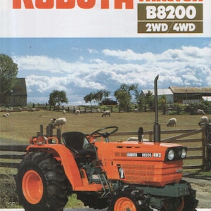 May include: A red and grey Kubota B8200 diesel tractor with a black steering wheel and a black seat. The tractor is in a field with a wooden fence and green grass. The sky is blue with white clouds.