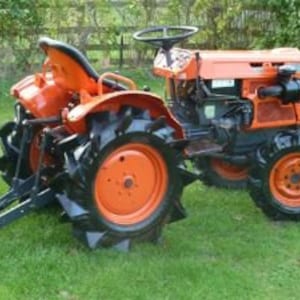 May include: An orange and black compact tractor with a black seat and a black steering wheel. The tractor has a rear hitch and a set of rear wheels with black tires.