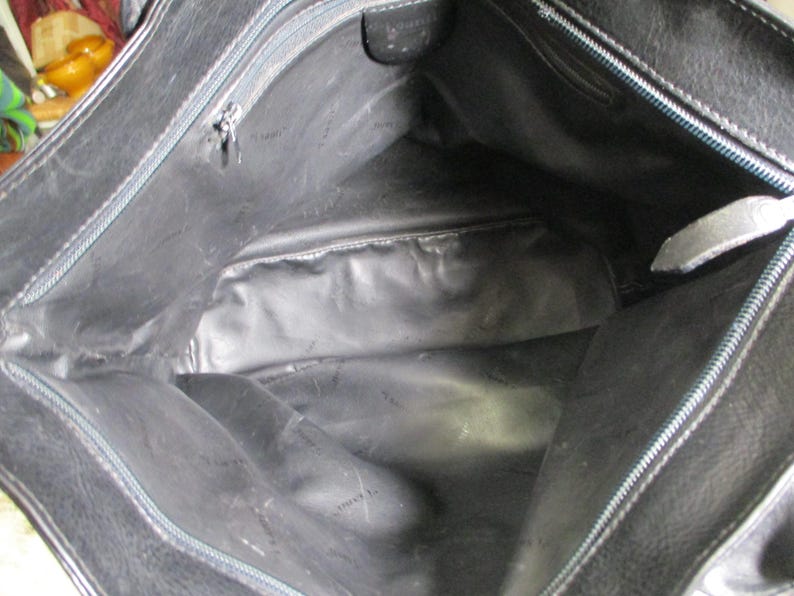 May include: The inside of a black leather tote bag with a zipper closure. The bag has a black fabric lining.