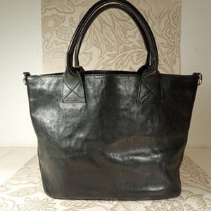 May include: A black leather tote bag with two top handles and a zipper closure.