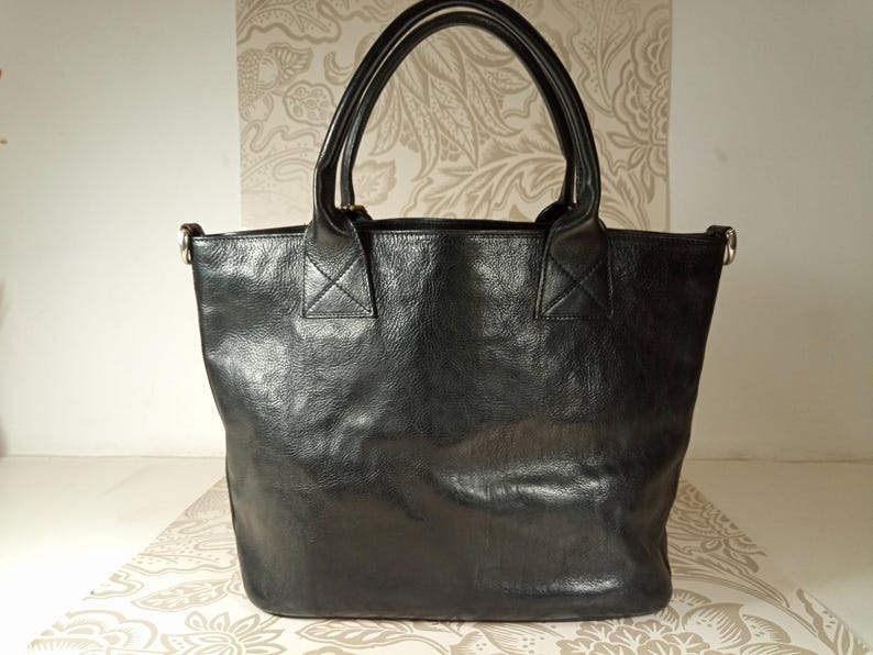 May include: A black leather tote bag with two top handles and a zipper closure.