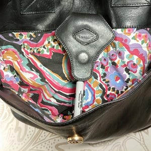 May include: Black leather tote bag with a paisley patterned lining. The bag has a flap closure with a metal button and a leather strap with a metal buckle.