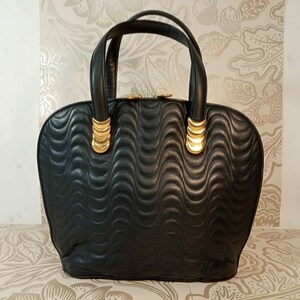 May include: A black handbag featuring a quilted wave pattern across the surface. The bag has two rounded handles attached with gold-toned metal hardware. The top closure is secured with two gold-toned circular zipper pulls.