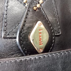 May include: Close-up of a black leather handbag with a gold-colored tag that reads "i santi".