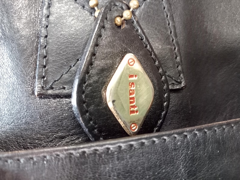 May include: Close-up of a black leather handbag with a gold-colored tag that reads "i santi".