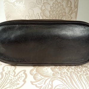 May include: Black leather tote bag with a smooth, flat bottom. The bag is empty and sitting on a patterned surface.