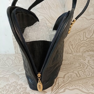 May include: A black quilted leather handbag featuring a curved silhouette, two top handles, and a gold-toned zipper pull with embossed text. The interior is partially visible, containing clear bubble wrap, and the exterior has a wavy stitched pattern.