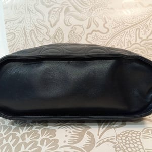 May include: A black handbag featuring a smooth, solid base and a top section adorned with a quilted, curved, wave-like pattern. The bag has a structured, rounded shape with defined piping along the edges, showcasing a consistent dark color palette.