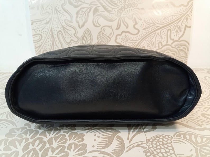 May include: A black handbag featuring a smooth, solid base and a top section adorned with a quilted, curved, wave-like pattern. The bag has a structured, rounded shape with defined piping along the edges, showcasing a consistent dark color palette.
