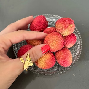 May include: A close-up of a bowl of lychees. The lychees are red and have a rough texture. The bowl is clear glass with a decorative pattern.