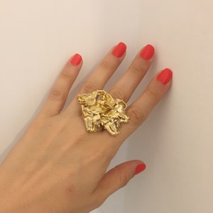 May include: A gold ring with a unique, abstract design. The ring is made of multiple pieces of gold that are intertwined and shaped into a cluster.
