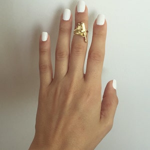 May include: A hand with white nail polish is wearing a gold ring with a unique abstract design.