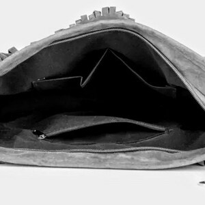 May include: A gray suede handbag with fringe detailing. The bag is open and shows a black interior with multiple pockets.
