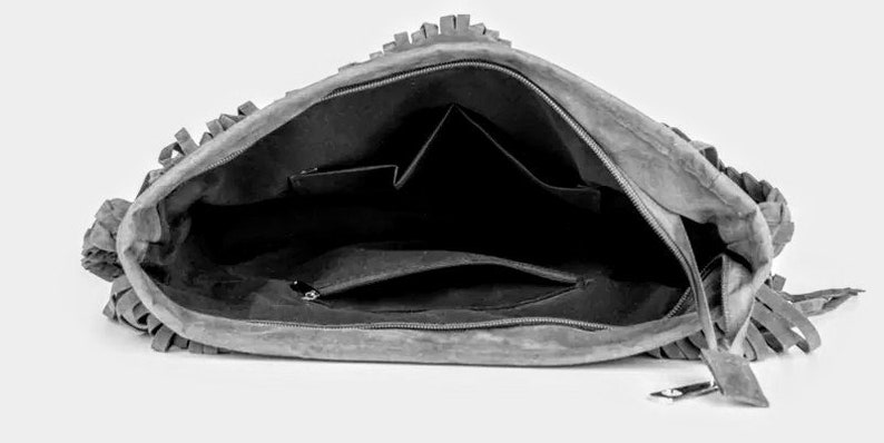 May include: A gray suede handbag with fringe detailing. The bag is open and shows a black interior with multiple pockets.