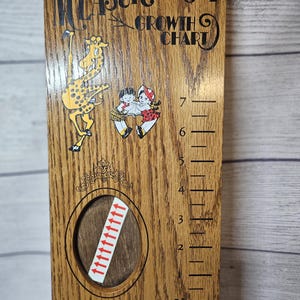 May include: Wooden growth chart with the text "Measure-Mate Growth Chart." Features illustrations of a giraffe and children. Includes a Sixth Grade label and height markings in feet.