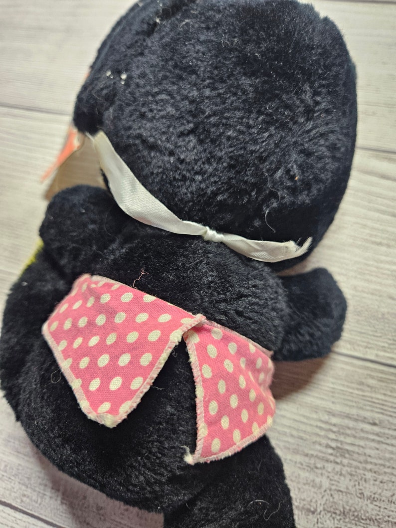 May include: A vintage black plush toy with a white ribbon and a pink polka dot scarf. The plush toy is made of a soft, fuzzy material and has a classic design. The toy is in good condition and would make a great addition to any collection.