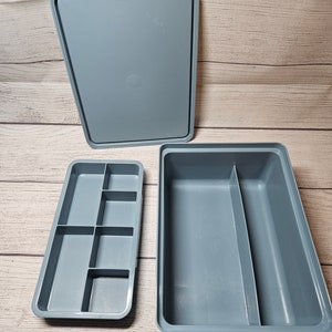 May include: A gray plastic storage container set consisting of a rectangular base with a single central divider, a removable tray featuring six small compartments of varying sizes, and a matching solid gray rectangular lid.