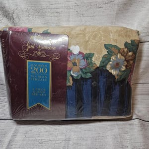 May include: A 4-piece queen bed set in plastic packaging. The bedding features a floral pattern with blue, pink, and green flowers on a tan background, with dark blue vertical stripes. The label reads Royale Gold Collection 200 Thread Count.