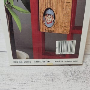 May include: A wooden photo frame with a red border, featuring a child's photo and a ruler-like measurement scale. The frame includes the text "First Grade" and "Pre-School". The bottom of the frame has the text "ITEM NO: 57300C &copy;1985 JUSTEN MADE IN TAIWAN R.O.C."