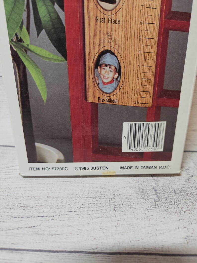 May include: A wooden photo frame with a red border, featuring a child's photo and a ruler-like measurement scale. The frame includes the text "First Grade" and "Pre-School". The bottom of the frame has the text "ITEM NO: 57300C &copy;1985 JUSTEN MADE IN TAIWAN R.O.C."