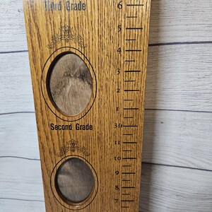 May include: Wooden growth chart with photo openings for First, Second, and Third Grade. The chart has a ruler with measurements in feet and inches. The wood has a natural grain and a light brown color.