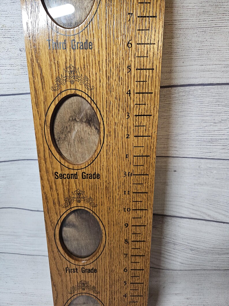 May include: Wooden growth chart with photo openings for First, Second, and Third Grade. The chart has a ruler with measurements in feet and inches. The wood has a natural grain and a light brown color.