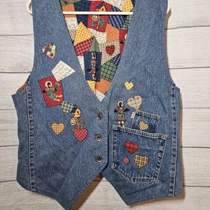 May include: A blue denim vest featuring a multi-colored patchwork lining with various patterns. The exterior is decorated with several fabric heart appliques, a small birdhouse, and a figure of a person. The text reads If Friends Were Flowers I'd Pick You.