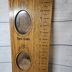 May include: Wooden growth chart with two oval photo frames and height markings. The chart has the words "Third Grade" and "Second Grade" above and below the frames. The height markings are in feet and inches.