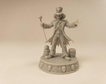 Puede incluir: Una figura miniatura de resina gris de un maestro de ceremonias esquelético con sombrero de copa con emblema de calavera, abrigo largo desgarrado y pajarita. La figura sostiene un bastón con calavera sobre una base circular con diamantes.