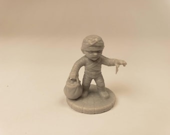 Puede incluir: Una pequeña figura de resina de color gris claro sin pintar de un personaje momia. La figura está envuelta en vendas, se apoya sobre una base circular con textura de adoquines y sostiene un pequeño saco en una mano mientras extiende la otra.