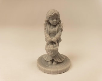 Puede incluir: Una pequeña figura de resina gris monocromática de un personaje con cabello largo, que viste una chaqueta y una falda, de pie sobre una base circular. El personaje sostiene una cesta llena de objetos redondos, con un pequeño detalle de estrella al frente.