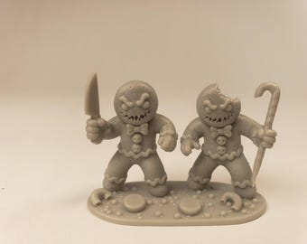 Puede incluir: Una figura de resina gris con dos personajes tipo pan de jengibre con expresiones de enfado. Un personaje sostiene un cuchillo, mientras que el otro sostiene un bastón de caramelo y tiene un mordisco en la cabeza. Ambos sobre una base texturizada.
