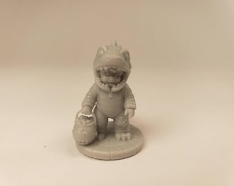 Puede incluir: Una pequeña figura de color gris monocromático que representa a un niño con un disfraz de dinosaurio con una capucha en forma de cabeza de dinosaurio. El niño está de pie sobre una base circular y sostiene un pequeño cubo redondo lleno de objetos esféricos texturizados.