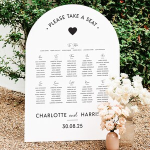 May include: A white arch-shaped seating chart with black text and a small black heart. The chart lists guest names for a wedding reception with the names "Charlotte and Harris" and the date "30.08.25".