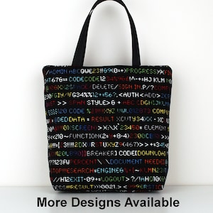 May include: A black tote bag featuring a colourful code design. The code includes letters, numbers, and symbols. The text "More Designs Available" is printed below the bag.