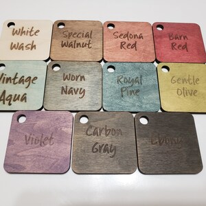 May include: A selection of square wooden colour samples, each with a small hole for hanging. Colours include White Wash, Special Walnut, Sedona Red, Barn Red, Vintage Aqua, Worn Navy, Royal Pine, Gentle Olive, Violet, Carbon Gray, and Ebony.