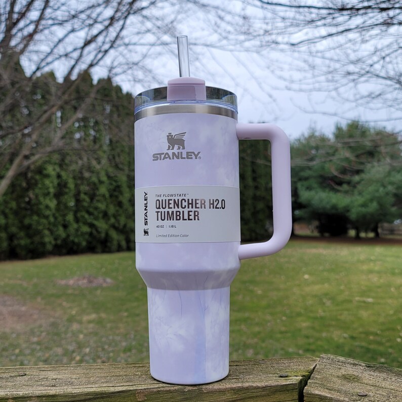 May include: A light purple Stanley Quencher H2.0 Tumbler with a handle and a clear straw. The tumbler has a marbled design and the text "QUENCHER H2.0 TUMBLER" is visible. It holds 40 oz.