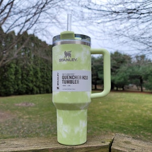 May include: A green and white tie-dye Stanley Quencher H2.0 tumbler with a handle and straw. The tumbler has a 40 oz capacity. The Stanley logo is visible on the front. The tumbler is a limited edition color.