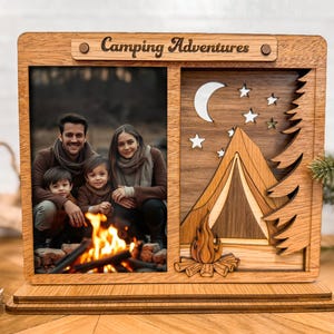 May include: Wooden photo frame with the words "Camping Adventures" at the top. The frame has two sections: one for a photo of a family and the other with a camping scene with a tent, campfire, moon, stars, and trees.