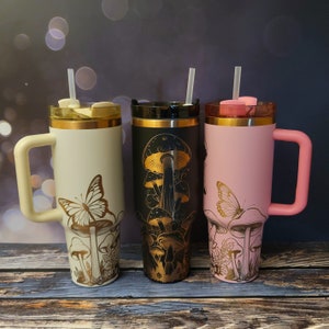 May include: Three stainless steel tumblers with lids and straws. The tumblers are decorated with a gold mushroom and butterfly design. The tumblers are white, black, and pink.