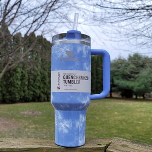 May include: A blue and white Stanley Quencher H2.0 Tumbler with a handle and straw. The tumbler has a marbled design and the text "QUENCHER H2.0 TUMBLER" is visible. It holds 40 oz (1.18 L).