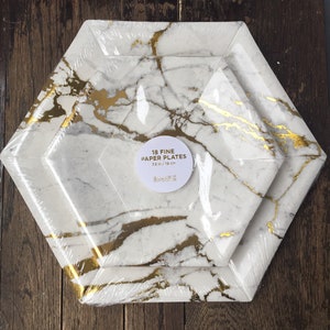 May include: A stack of 18 fine paper plates with a marble design in white and gold. The plates are 7.5 inches in diameter. The plates are packaged in plastic wrap.