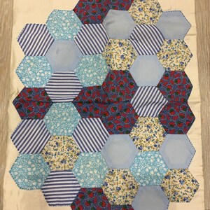 May include: A patchwork quilt with a hexagonal pattern. The quilt is made of various fabrics with blue, white, red, and floral patterns.