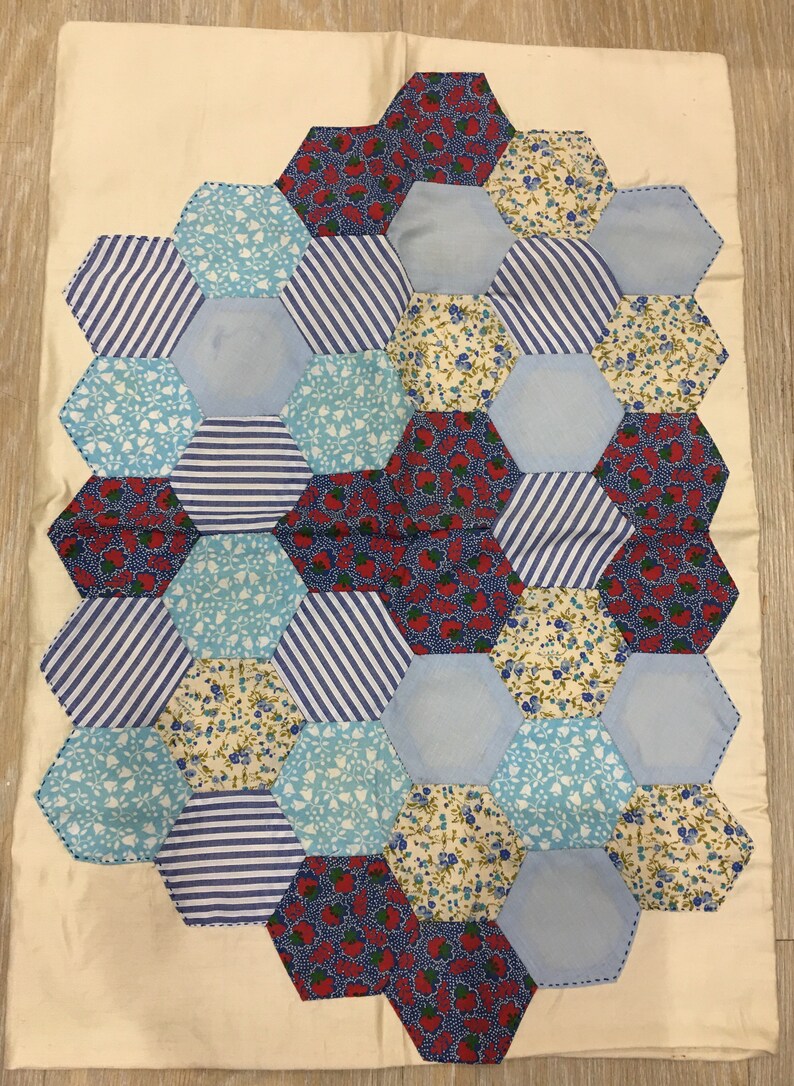 May include: A patchwork quilt with a hexagonal pattern. The quilt is made of various fabrics with blue, white, red, and floral patterns.