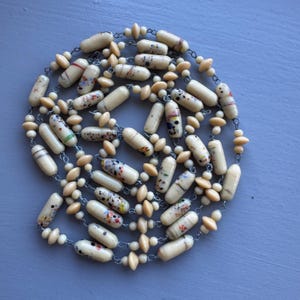 May include: A long necklace made of cream-coloured glass beads with colourful speckles. The beads are interspersed with smaller, round, cream-coloured beads. The necklace is strung on a silver chain.