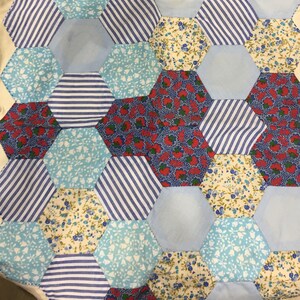 May include: A patchwork quilt with a hexagonal pattern. The quilt is made of various fabrics with floral and striped designs in shades of blue, red, and white.