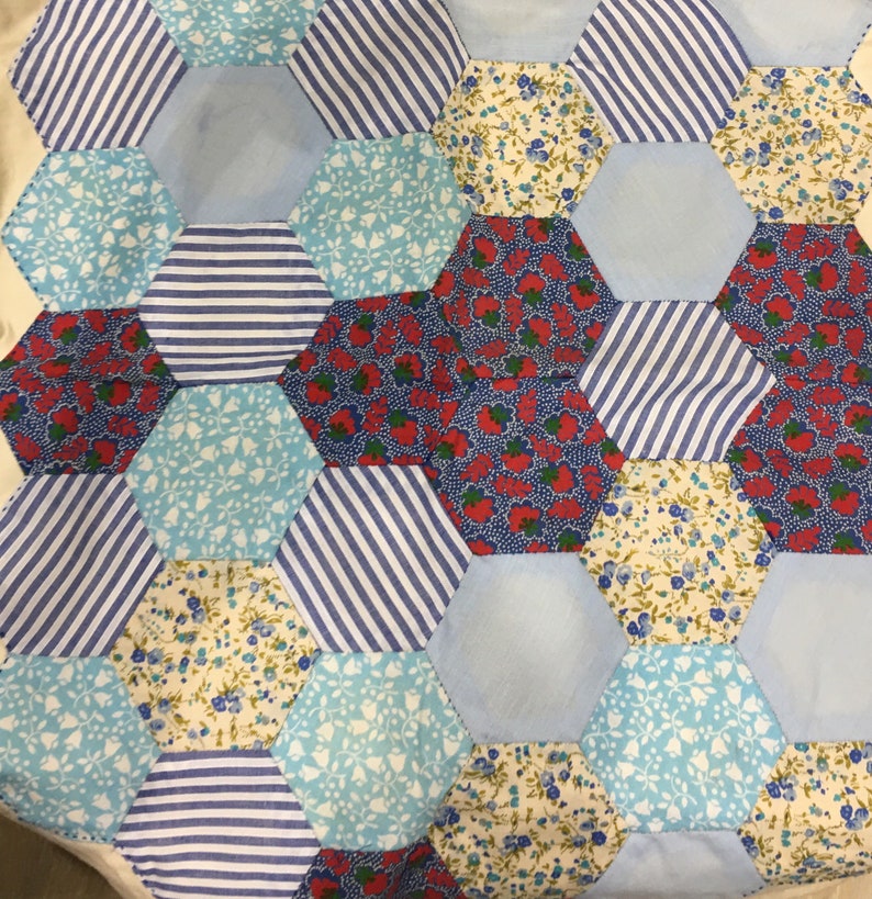 May include: A patchwork quilt with a hexagonal pattern. The quilt is made of various fabrics with floral and striped designs in shades of blue, red, and white.