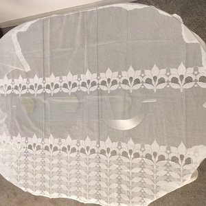 May include: White lace tablecloth with a delicate floral pattern. The tablecloth is oval shaped and has a scalloped edge.