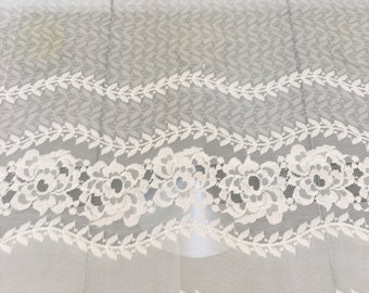 May include: Off-white lace fabric with a floral and leaf pattern. The lace features a scalloped edge and is semi-transparent, allowing light to pass through. The design includes detailed floral motifs and delicate leaf borders.
