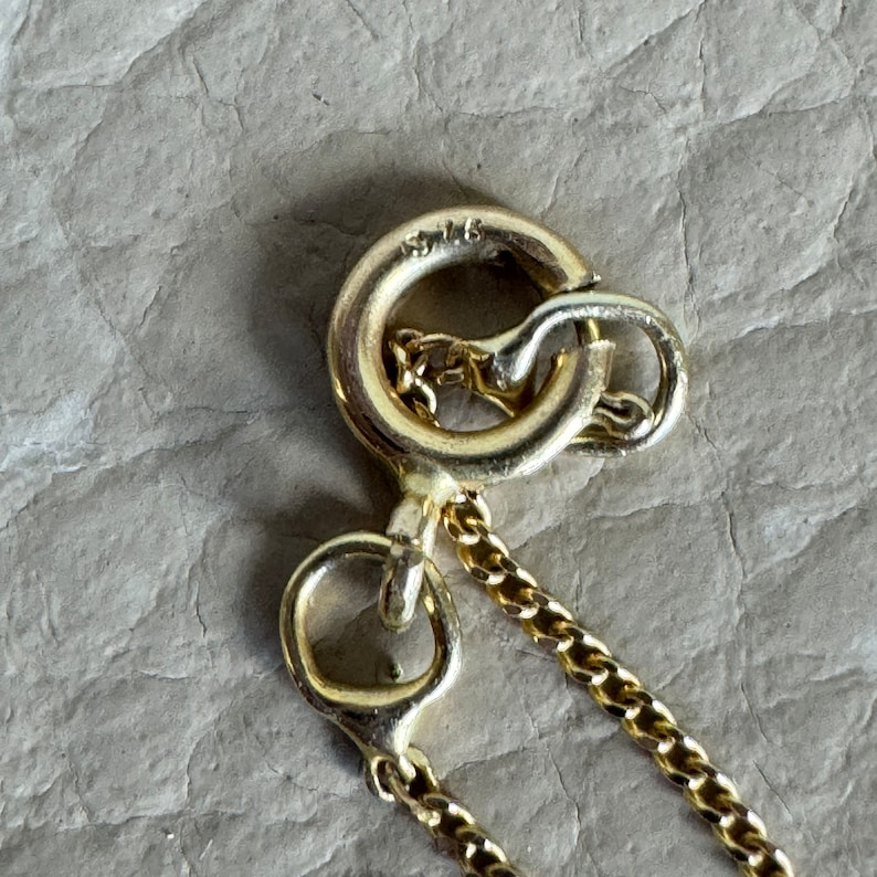 May include: Gold chain necklace with a lobster clasp closure. The clasp has the inscription "925" on it.